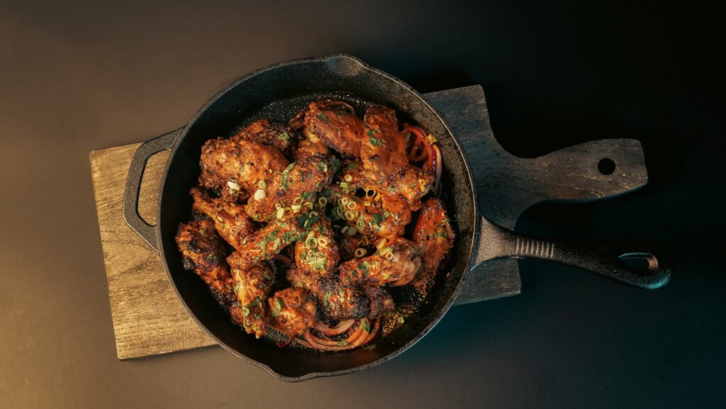 Delicious spicy chicken wings served in a cast iron skillet with garnishes.